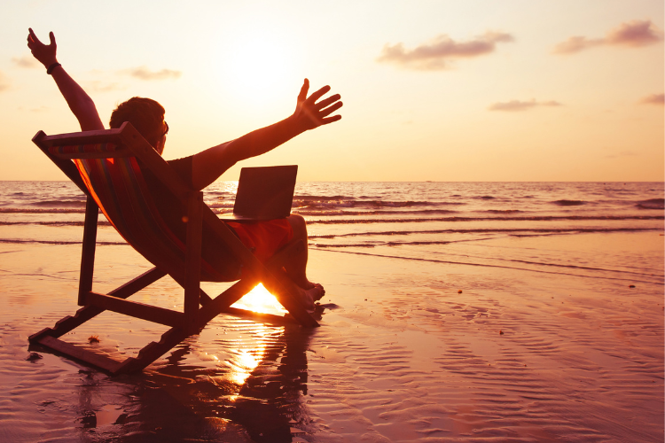 man sitting on beach chair at sunset with laptop