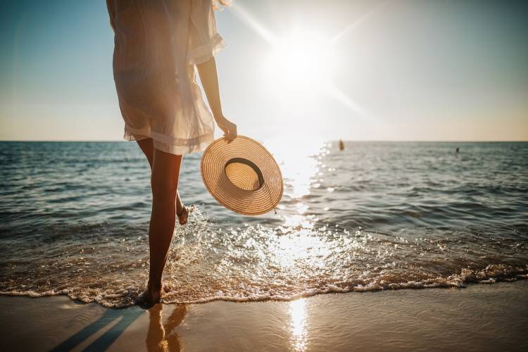 woman walking on beach with sun hat in hand