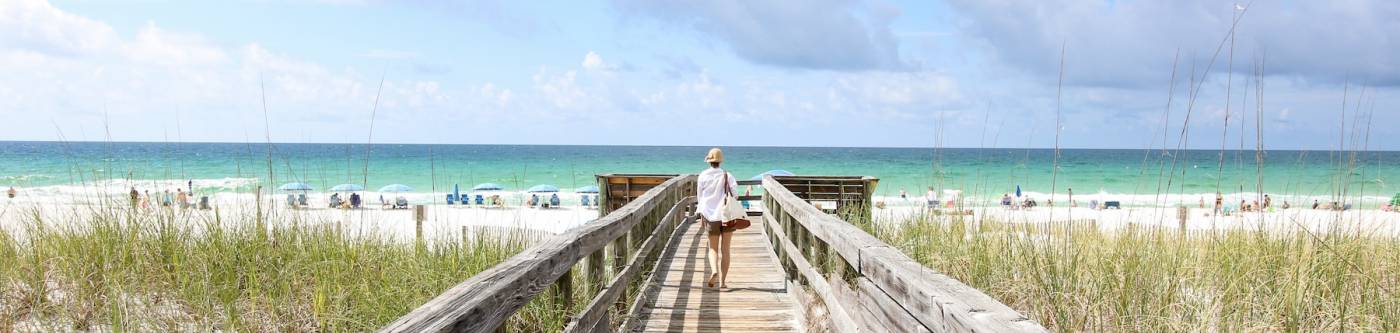 woman walking on boardwalk toward beach 